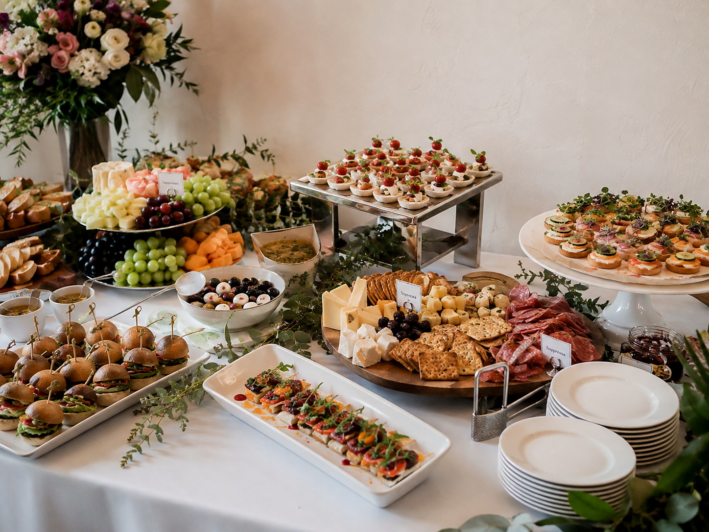 Mesa de entremeses y catering con mini sándwiches, quesos, frutas y canapés